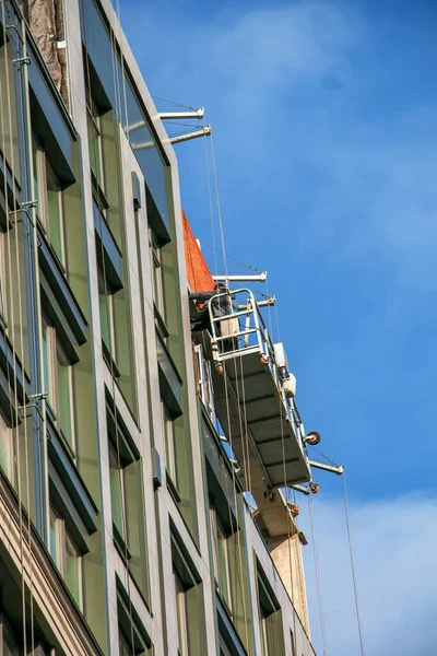 Suspended platform, construction cradle hanging on building. Installation and repair work. Building facades construction works. Facade of high-rise building under construction, finishing works