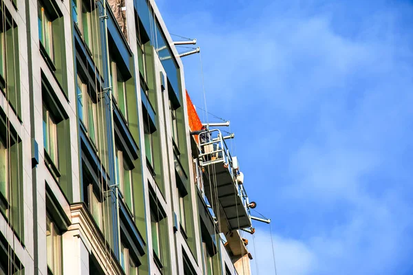 Suspended platform, construction cradle hanging on building. Installation and repair work. Building facades construction works. Facade of high-rise building under construction, finishing works