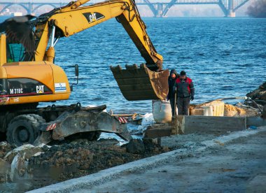 Dnepropetrovsk, Ukrayna - 11.26.2021: Kazıcı seti güçlendirmek için çalışıyor. Nehir kıyısında çalışan hidrolik kazıcı.