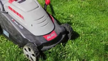 Bir adam yeşil çimenlikte çim biçer, çim biçme makinesiyle.