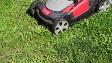 Bir adam yeşil çimenlikte çim biçer, çim biçme makinesiyle.