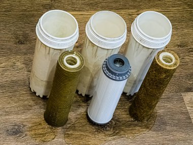Toprak, kil ve kirletici madde kalıntıları olan üç adet kullanılmış su filtresi. Çok aşamalı su filtresi kartuşları değiştiriliyor.