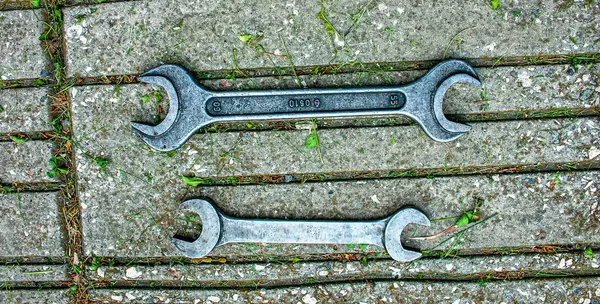 Double open-end wrenches of different sizes on a tiled sidewalk.
