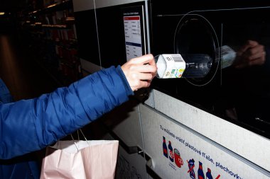 Nitra, Slovakya - 01.16.2024: Bir adamın elindeki şişeyi atık geri dönüşüm makinesine koymak.