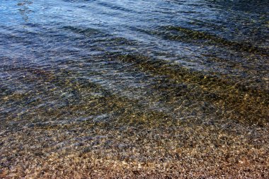 Traunsee Gölü 'nün kıyı bölgesindeki sularının arka planı. Suyun altındaki taşların renkli dokusu.