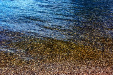 Traunsee Gölü 'nün kıyı bölgesindeki sularının arka planı. Suyun altındaki taşların renkli dokusu.