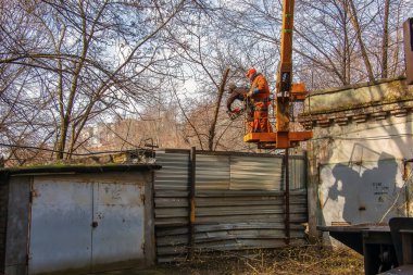 Dnepr, Ukrayna - 03.20.2024: Belediye çalışanları vinç sepetinde elektrikli testere ve tehlikeli ağaçları budamak için duruyorlar.