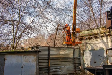 Dnepr, Ukrayna - 03.20.2024: Belediye çalışanları vinç sepetinde elektrikli testere ve tehlikeli ağaçları budamak için duruyorlar.