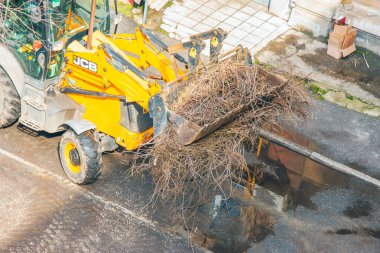 Dnepr, Ukrayna - 03.20.2024: Bir buldozer ağaçları budadıktan sonra dalları toplar. Yukarıdan görüntüle.