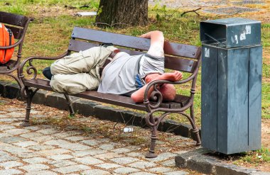 Nitra, Slovakya - 05.26.2024: Evsiz bir adam sokakta bir bankta uyuyor.