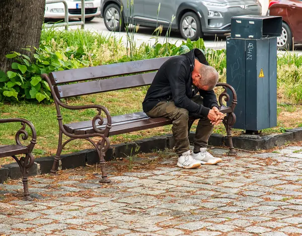 Nitra, Slovakya - 05.26.2024: Evsiz bir adam sokakta bir bankta uyuyor.