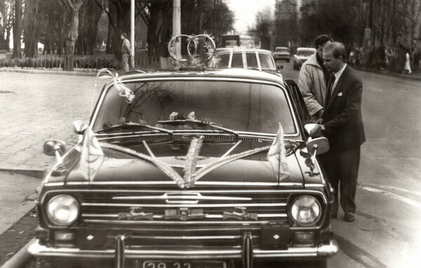 Dnepropetrovsk, USSR - November 14, 1992: Vintage portrait of a young man groom before the wedding near the car decorated with wedding decorations.