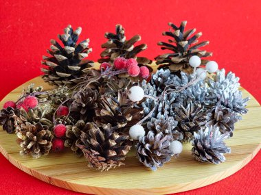 Yaratıcılık için yeni yıl seti. Koniler, boyanmış koniler ve tahta bir tahtanın üzerinde jöleli böğürtlenler. Kırmızı arka plan. Yakın plan..