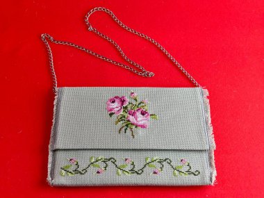 Kırmızı arka planda el yapımı retro çanta. Çantanın yüzeyinde çapraz dikiş var. Gül süsü. Zincir saplı eski bir çanta..