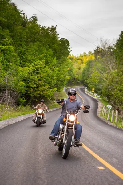 İki arkadaş kır yolunda motosiklet sürüyor.