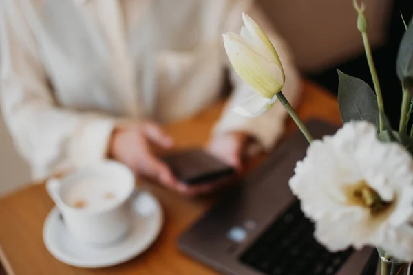 Faceless beautiful young or mature professional career woman boss working on laptop. Modern women entrepreneur working in restaurant and cafe small business. Focus on flower. Blurred background.
