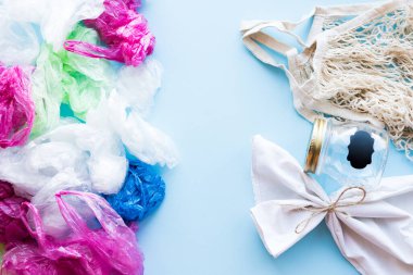 Many disposable plastic bags vs reusable cotton bags and glass jar on a blue background. Zero waste shopping. Sustainable living, plasticfree concept. Eco friendly plastic free items. Top view.