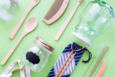 Sıfır atık. Pamuk torbası, bambu çatal bıçak takımı ve diş fırçası, cam kavanozlar, yeşil arka planda metal ve bambu pipetler. Sürdürülebilir yaşam. Eko dostu plastik eşyalar. Üst görünüm.
