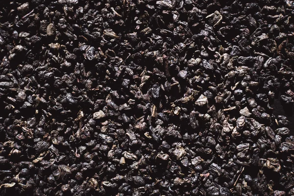 Black tea texture background. Black dried tea leaves, marco. Pattern of black tea leaves on a flat surface.