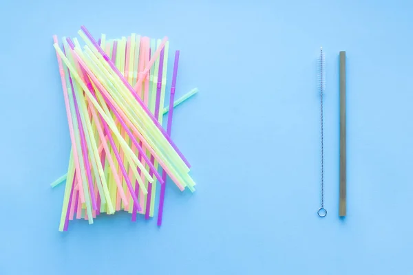 Many plastic drinking straws vs one reusable bamboo drinking straw on a blue background. Zero waste sustainable living, plasticfree concept. Eco friendly plastic free items. Top view.