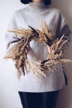 Şık bir sonbahar çelengi. Kuru otlardan, kır çiçeklerinden ve buğdaydan kırsal çelenk tutan kadın elleri. Sonbahar tatili atölyesi. Çiçekçi boho çelengi yapıyor.. 
