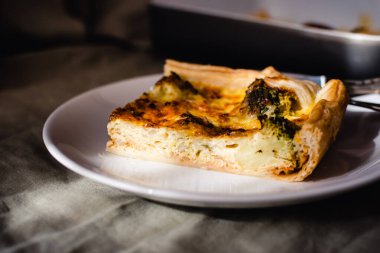 Sliced traditional french open quiche pie with cheese and broccoli on light linen background. A piece of vegetable quiche with broccoli and cheese. Vegetarian pie. High quality photo.