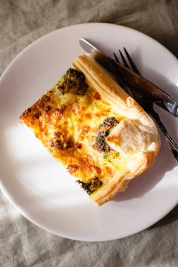 Sliced traditional french open quiche pie with cheese and broccoli on light linen background. A piece of vegetable quiche with broccoli and cheese. Vegetarian pie. Top view. High quality photo. 