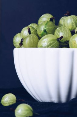 Gooseberry Harvest, a crop of ripe gooseberries. Berries of gooseberry close-up. Fresh gooseberries on dark background. Fresh gooseberries in white bowl on black stone slate background.