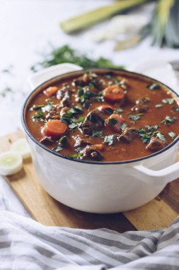 Gri arka planda patates, havuç ve baharatla pişirilmiş sığır eti eti. Modern tasarım dökme demir kızartma kabında geleneksel domates soslu güveç. Yüksek kalite fotoğraf.