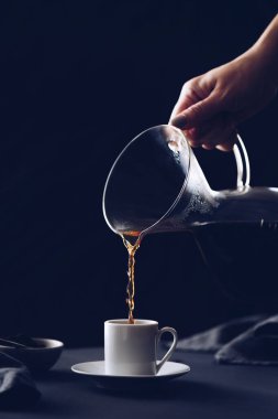Filtre damlatıcıyla kahve yapmak. Kağıt filtreden damlayan kahve. Kahve yapmak için alternatif bir yol. Makro yakın çekim. Siyah arka planda cam çaydanlıktan beyaz fincana kahve dökülüyor..