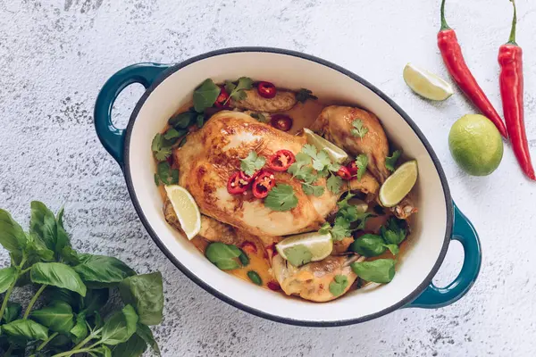 Whole skillet chicken with lime, red hot chilly pepper, coriander and coconut milk in a cast iron casserole. Roasted whole chicken with basil in a cast iron skillet pot. Top view. High quality photo.