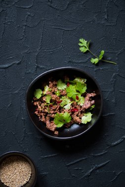 Baharatlı carpaccio salatası, yeşil kişniş, limon ve siyah arka plandaki siyah kasede kırmızı acı biber. Çin yemeği tarifi. Restoran menüsü. Üst Manzara. Düz yatıyordu.