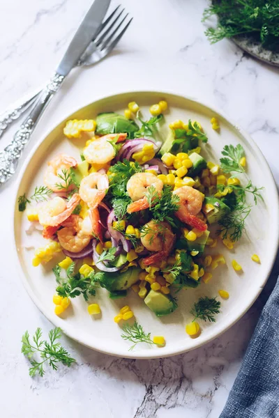 Healthy salad with fresh vegetables - corn, avocado, red onion, shrimp and coriander on a white plate. Vegetarian food recipe. Diet fitness menu. Flat lay. Top view on marble background.