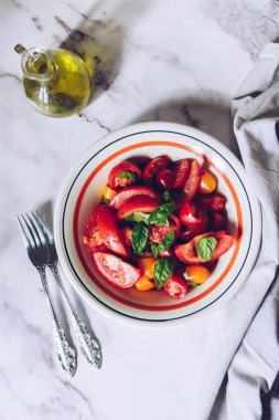 Beyaz mermer arka planda farklı türde domates ve fesleğen içeren sağlıklı bir salata. Domates salatası. Vejetaryen vejetaryen yemek tarifi. Diyet fitness menüsü. Üst Manzara. Düz yatıyordu.