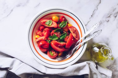 Beyaz mermer arka planda farklı türde domates ve fesleğen içeren sağlıklı bir salata. Domates salatası. Vejetaryen vejetaryen yemek tarifi. Diyet fitness menüsü. Üst Manzara. Düz yatıyordu.