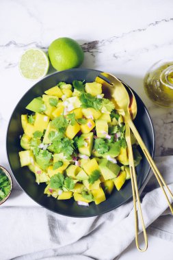 Sağlıklı salata, avokado, mango, kırmızı soğan ve yeşil kişniş ile siyah tabakta yeşil mermer arka planda limon ve zeytinyağı. Vejetaryen yemek tarifi. Diyet fitness menüsü. Üst Manzara. Düz yatıyordu.