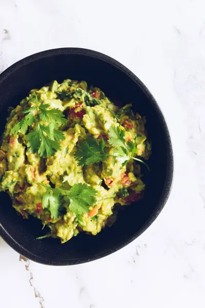 Bir kase guacamole. Meksika mutfağından taze sebze, avokado, domates, limon, yeşil kişniş ve yeşil soğanlı sağlıklı bir şekilde yayılmış. Vejetaryen vejetaryen yemek tarifi. Diyet fitness menüsü. Üst görünüm.