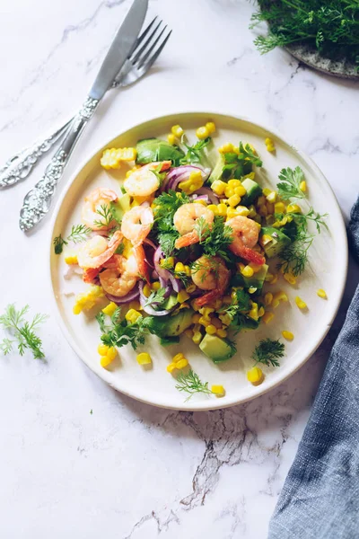 Healthy salad with fresh vegetables - corn, avocado, red onion, shrimp and coriander on a white plate. Vegetarian food recipe. Diet fitness menu. Flat lay. Top view on marble background.