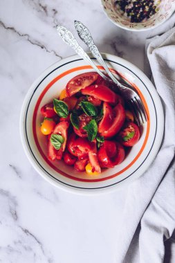 Beyaz mermer arka planda farklı türde domates ve fesleğen içeren sağlıklı bir salata. Domates salatası. Vejetaryen vejetaryen yemek tarifi. Diyet fitness menüsü. Üst Manzara. Düz yatıyordu.