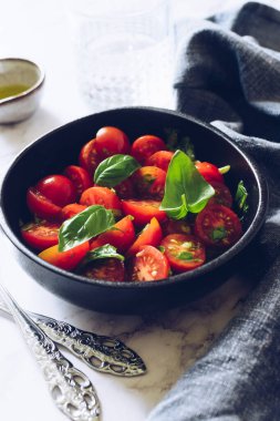 Beyaz mermer arka planda kiraz domatesli sağlıklı salata ve fesleğen. Domates salatası. Vejetaryen vejetaryen yemek tarifi. Diyet fitness menüsü. 