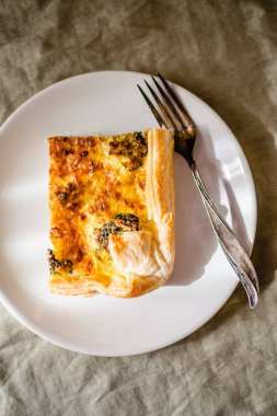 Sliced traditional french open quiche pie with cheese and broccoli on light linen background. A piece of vegetable quiche with broccoli and cheese. Vegetarian pie. Top view. High quality photo. 