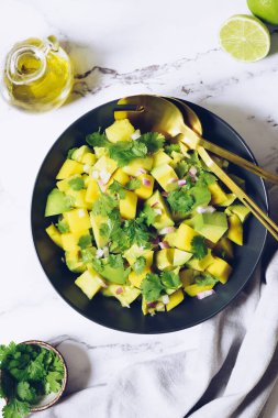 Sağlıklı salata, avokado, mango, kırmızı soğan ve yeşil kişniş ile siyah tabakta yeşil mermer arka planda limon ve zeytinyağı. Vejetaryen yemek tarifi. Diyet fitness menüsü. Üst Manzara. Düz yatıyordu.
