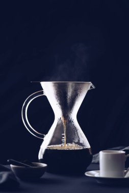 Filtre damlatıcıyla kahve yapmak. Kağıt filtreden damlayan kahve. Kahve yapmak için alternatif bir yol. Makro yakın çekim. Siyah arka planda cam çaydanlıktan beyaz fincana kahve dökülüyor..