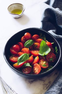 Beyaz mermer arka planda kiraz domatesli sağlıklı salata ve fesleğen. Domates salatası. Vejetaryen vejetaryen yemek tarifi. Diyet fitness menüsü. 