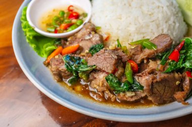 Balık soslu, kırmızı biberli, ahşap bir masada salatalık ve marullu fesleğenli kızarmış biftek..