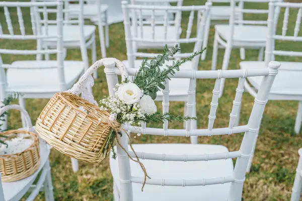 Düğünde çimenlerin üzerine beyaz sandalyeler, sepetin içinde düğün çiçekleri, vanue 'de bahçe düğün süsleri..