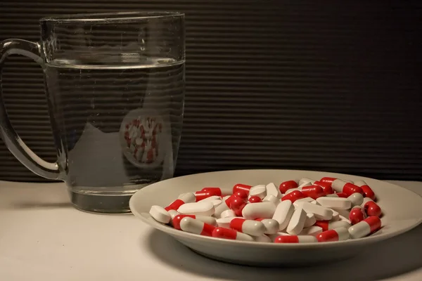 white and red pills in a plate. a glass of water. close-up. the concept of health, treatment.