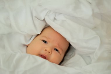 Yeni doğan bebek gülümser ve güler. Duygularını gösteriyor. Bebek beyaz bir kumaşın üzerinde yatıyor.