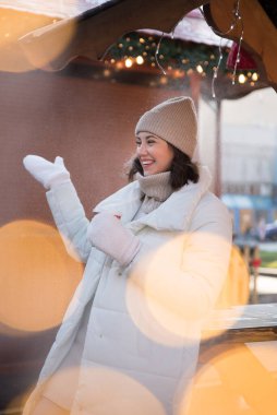 Adil. Beyaz ceketli ve beyaz şapkalı bir kız. Kız gülümsüyor. Elde bir fincan kahve. Ahşap yazlık. Kız seviniyor. duygular.