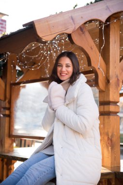 Adil. Beyaz ceketli ve beyaz şapkalı bir kız. Kız gülümsüyor. Elde bir fincan kahve. Ahşap yazlık. Kız seviniyor. duygular.